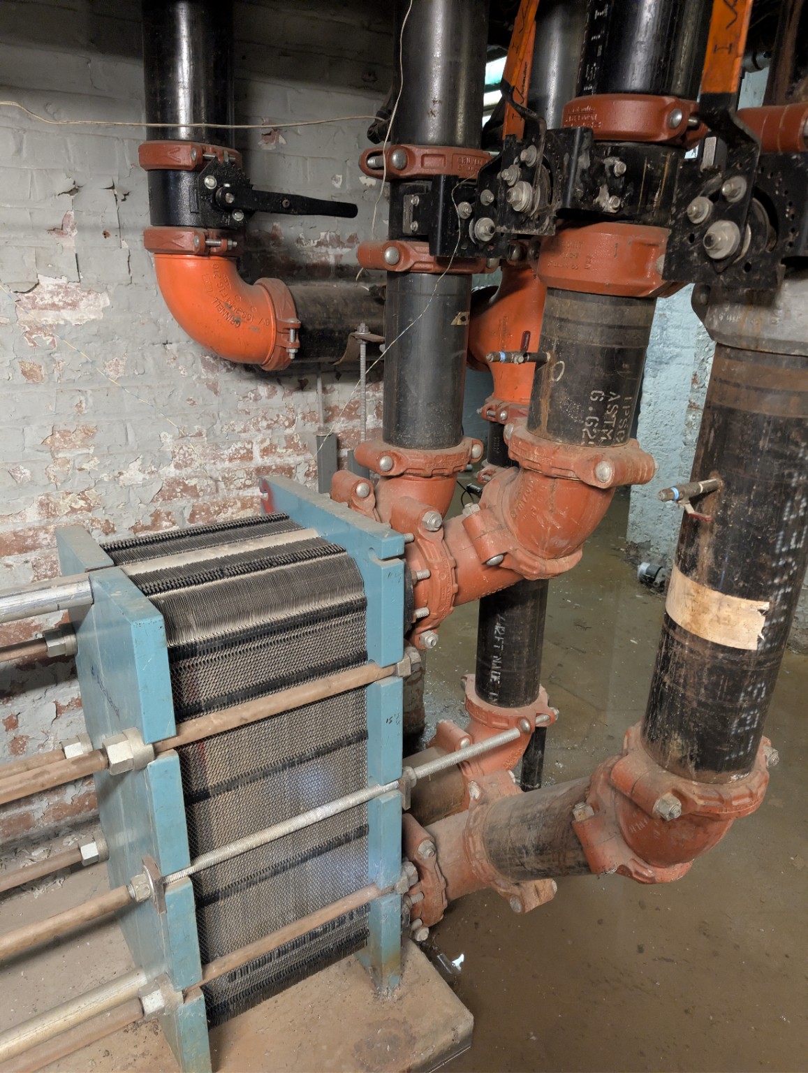 Heat exchanger connected to mechanical piping, orange couplings, and hand-operated valves.